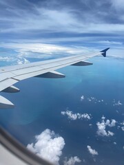 Fototapeta premium View from airplane window showing aircraft wing flying above deep blue ocean with scattered clouds. Travel, aviation, and vacation concept with copy space.