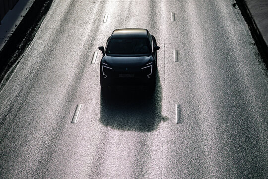 A black car with futuristic headlights is driving on a wet road, top view