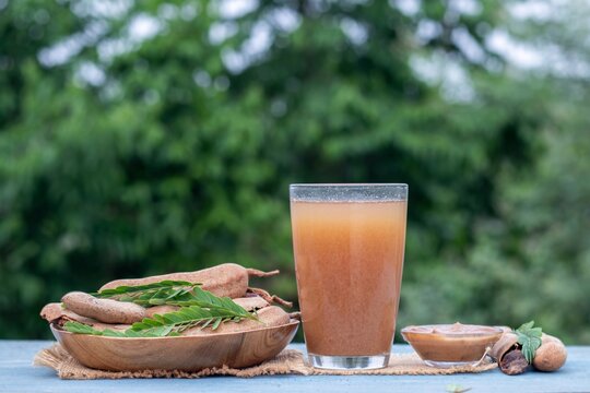 Ripe Tamarind Juice and Pods Fruit or Imli Fruit Sharbat or Juice Water in a Glass with Leaves Isolated on Wooden Background with Copy Space