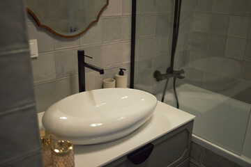 Fototapeta premium Modern bathroom interior featuring ceramic vessel sink with black faucet, soap dispenser on countertop, glass shower enclosure with bathtub, tiled walls in neutral tones
