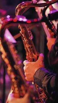 Close-up of a saxophonist's hand on a shiny brass saxophone. Vibrant purple and pink stage lights create a warm, energetic mood with soft bokeh. For music, arts, and entertainment concepts