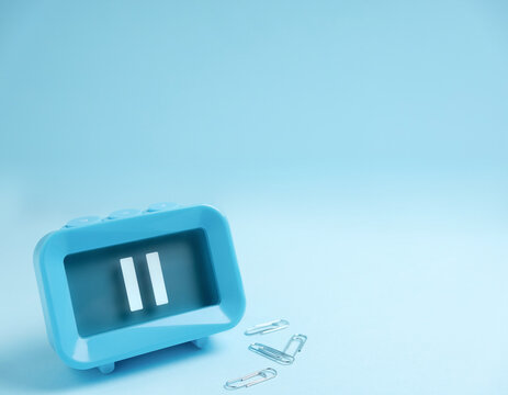 Blue alarm clock with a pause symbol on a light blue background, flat lay, plenty of copy space for time management and break concept.