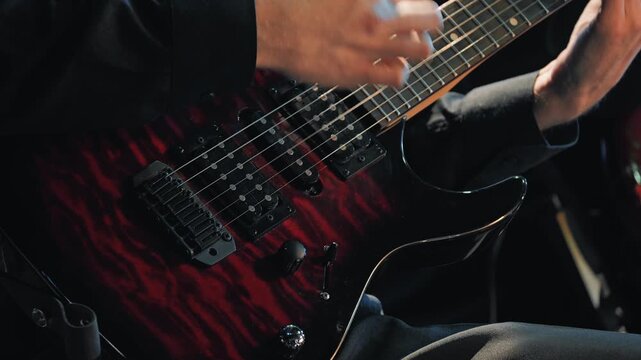 Dynamic close-up of a guitarist's hands playing a fast solo on a red and black electric guitar. Captures the energy of a live music performance at a concert or jazz club