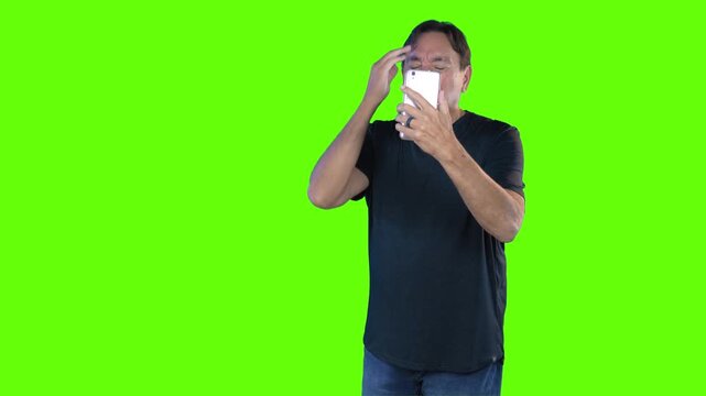 Frustrated man holding smartphone trying to get cellular service, confused expression against green screen background. Ideal for communication or tech issues concepts. 15102
