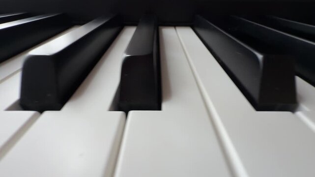 Smooth sliding shot along the black and white keys of a classical piano keyboard, revealing the elegant contrast and repeating pattern of the musical instrument in extreme close up