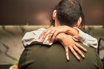 Obraz premium Caucasian man embracing Black woman, her arms wrapped around his neck, both standing closely together in kitchen setting, hands and back of man visible, intimacy expressed through gesture