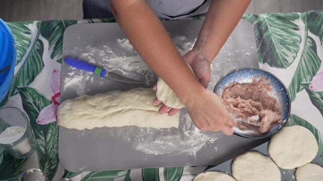 Woman shaping dough and filling pies with meat in cozy kitchen highlighting homemade recipe and traditional culinary process. High quality 4k footage