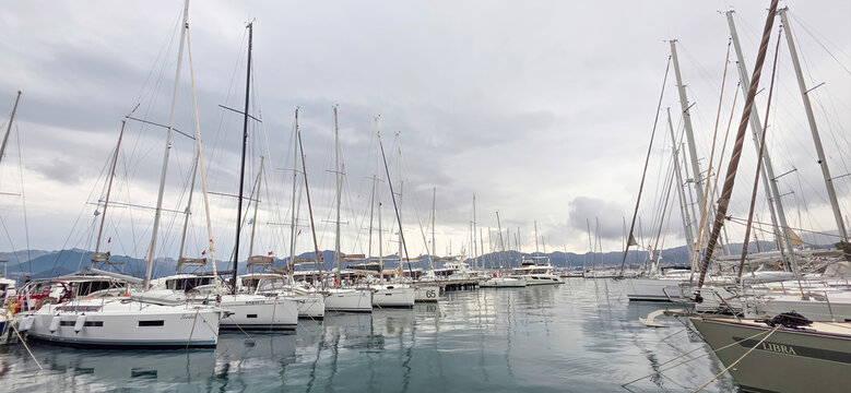 Sailboats docked in marina under cloudy sky with calm water reflections