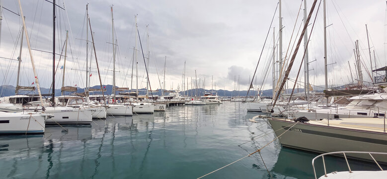 Sailboats docked in marina with cloudy sky and calm water reflections