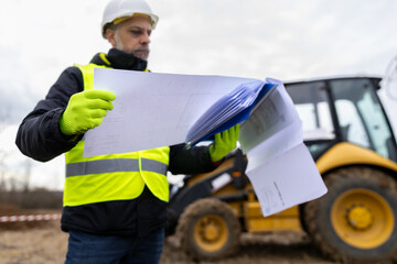 Fototapeta premium Construction supervisor examining blueprints at heavy equipment work site