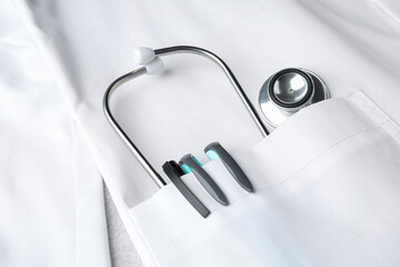 Doctor's white coat with stethoscope and pens on light background, closeup