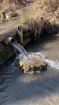 Storm drain releasing cloudy brown water into channel, concrete culvert with mossy edges, sediment churn and murky flow, environmental