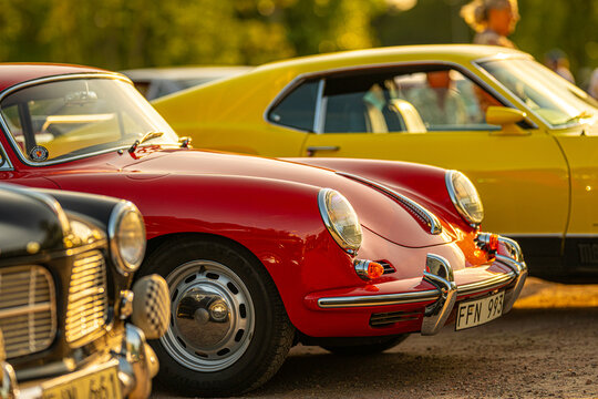 Gothenburg, Sweden - July 25 2024: 1960 Porsche 356 classic red coupe parked beside yellow muscle car at meet.