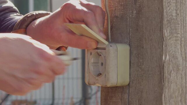 Realtime footage showing connection of electrical cable to outdoor weatherproof socket with background environment
