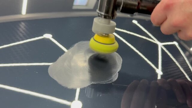 A car service worker polishes the car body with a polishing machine. Detailing and polishing of the car. Car detailing - hands with an orbital polishing machine in an auto repair shop. PDR. 