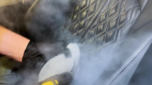 Car detailing and the concept of car interior care. The detailing master cleans the car interior with a hot steam cleaner close-up. Dry cleaning of the car interior, close-up, selective focus. 