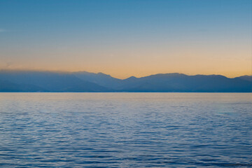 Obraz premium Mer calme bleue avec une chaîne de montagnes lointaine sous un ciel de coucher de soleil pastel au large de l'île de Capraia, Italie