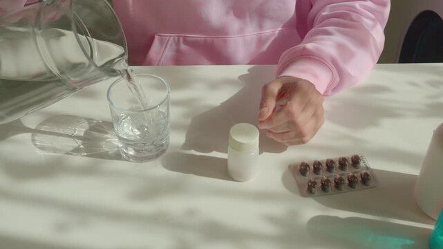 Woman taking menopause relief pill with glass of water at sunlit table