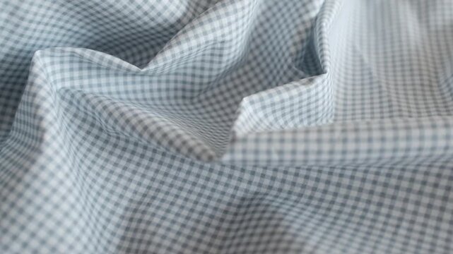 Close-up of soft blue and white gingham fabric texture with gentle folds and ripples. Classic checkered pattern textile background for fashion, home decor, and rustic themes.