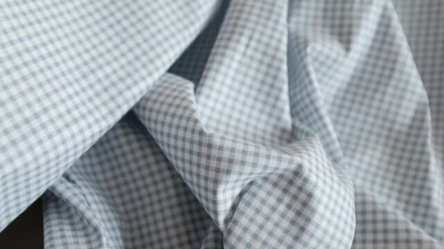 Close-up of soft blue and white gingham fabric texture with gentle folds and ripples. Classic checkered pattern textile background for fashion, home decor, and rustic themes.
