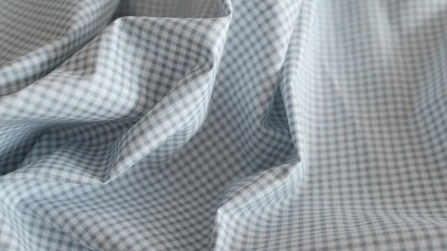 Close-up of soft blue and white gingham fabric texture with gentle folds and ripples. Classic checkered pattern textile background for fashion, home decor, and rustic themes.