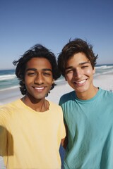 Obraz premium Two young adult males asian hispanic friends smiling at sunny beach with ocean waves wearing colorful tshirts and taking a selfie together