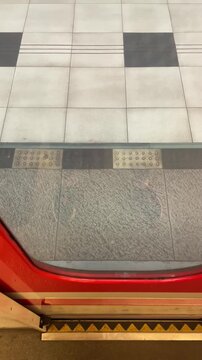 Platform reflection showing passenger shoes and train door threshold, polished glass mirror effect and yellow safety edge capture brief