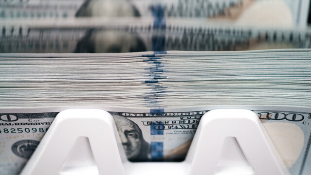 Money counting machine processing stacks of cash with detailed view of hundred-dollar bills and clear display, emphasizing currency handling and financial transactions