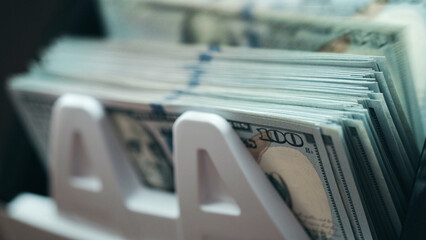 Fototapeta premium Close up of US dollar banknotes in money counting machine. Wealth, finance and accounting concept. 