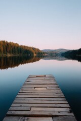 Fototapeta premium Wooden dock pier lake calm sunrise forest reflection tranquil morning mist horizon wooden planks leading into still water peaceful landscape