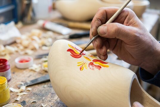 Artisan painting a traditional red and yellow floral pattern on a wooden shoe