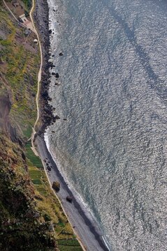 A high-angle view capturing the massive Cabo Girao cliffs, terraced farmland, and the sun-drenched, shimmering Atlantic waters of Madeira island.