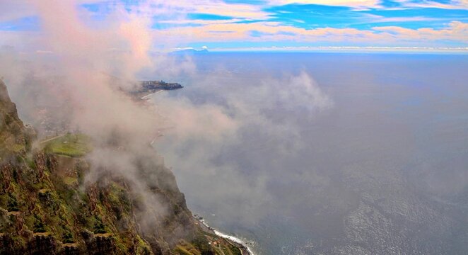 A dramatic, misty view from the high cliffs of Cabo Girao, Madeira, showcasing the steep coastline meeting the vast, serene Atlantic Ocean.