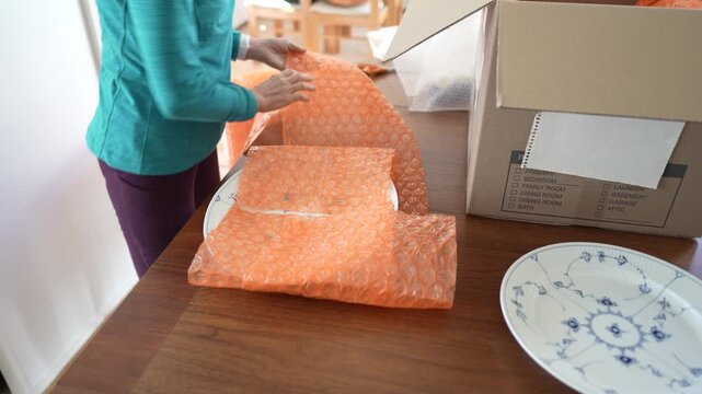 Mature woman packs china carefully in bubble wrap and a box for shipping to a family member.
