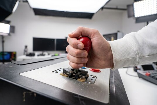 Hand holding the red ball of an arcade joystick installed on a metal control panel