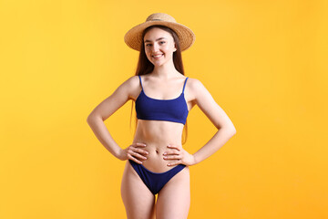 Beautiful young woman wearing stylish blue bikini and straw hat on yellow background