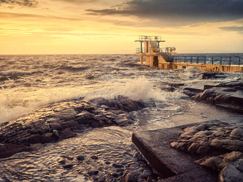 Famous Blackrock diving tower in Salthill, Galway city, Ireland. Tourist landmark and swimming area. Warm sunrise light and cloudy sky create unreal mood and atmosphere. Travel and tourism.
