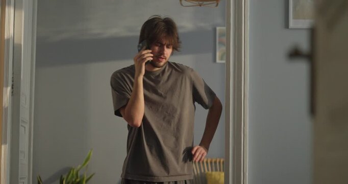 A man stands in a sunlit room, deep in conversation on the phone, sharing moments of joy and curiosity