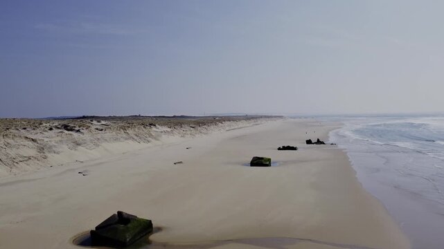 Forward drone movement above Cap Ferret beach showing German World War II blockhouses sinking into the sand far from the dune, highlighting ongoing coastal erosion driven by Atlantic Ocean forces
