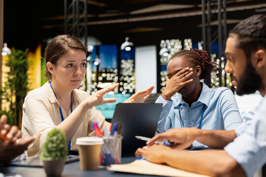 Manager in office doing layoffs after evaluating staff performance, giving bad news to depressed employees. Management dissatisfied with work done by diverse team, firing them after reviewing metrics