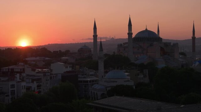 Istanbul, Turkey - 06.25.2023: The historic Hagia Sophia mosque with tall minarets is illuminated by a bright sunrise over Istanbul city. Warm golden light spreads across the skyline, highlighting