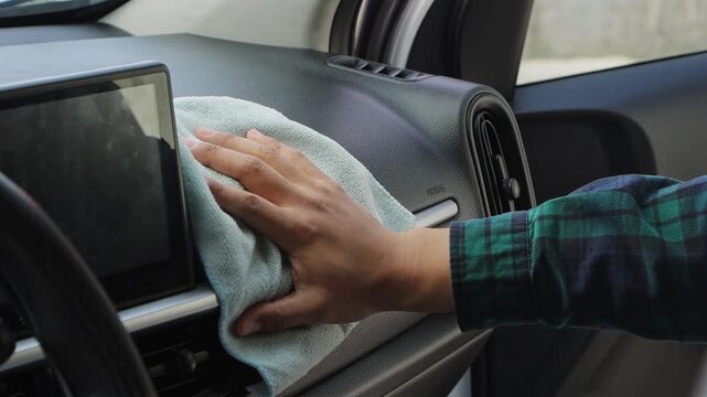 Close up of a hand cleaning the car console with a cloth, representing interior care, maintenance, and hygiene.
