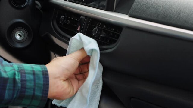Close up of a hand cleaning the car dashboard console using a cloth, showing vehicle care, interior hygiene, and maintenance routine.