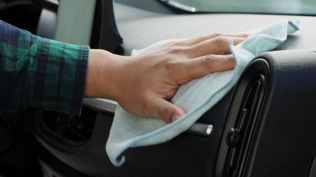 Close up of hands wiping a car center console, showing interior cleaning, hygiene, and vehicle maintenance routine.