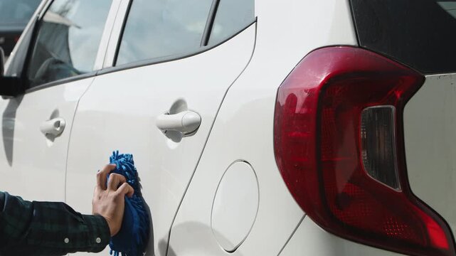 Close up of a man cleaning a car door using a cloth, representing vehicle care, maintenance, and outdoor cleaning activity.