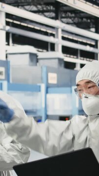 Vertical video Engineering team working together in semiconductor production plant floor to do maintenance on manufacturing machinery. Coworkers in safety gear collaborating to do checkup on PCB