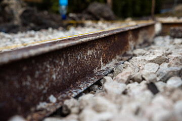 Fototapeta premium A rusted steel rail sits in coarse ballast, pitted and flaked. Shallow depth of field keeps stones sharp and distance soft, daylight tones suggest an outdoor work zone.
