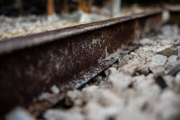 Fototapeta premium Low angle macro view shows a corroded steel rail beside pale ballast, a thin painted line on top, daylight and shallow depth of field isolate gritty industrial detail.
