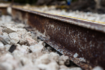 Fototapeta premium Ground level view shows a corroded steel rail, pale angular ballast, and a thin safety line. Late daylight, shallow depth of field, and muted tones emphasize decay.
