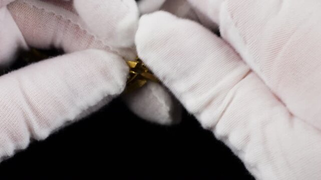 Close-up of vintage gold-tone bracelet being examined in white cotton jersey gloves. This elegant piece of jewelry features detailed metalwork set with sparkling white crystals.